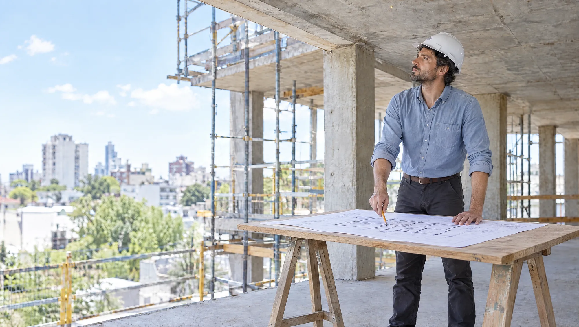 Un Arquitecto de Estudio TREO compara el plano extendido sobre una mesa de obra con la estructura de hormigón de un edificio en construcción de la Ciudad de Buenos Aires